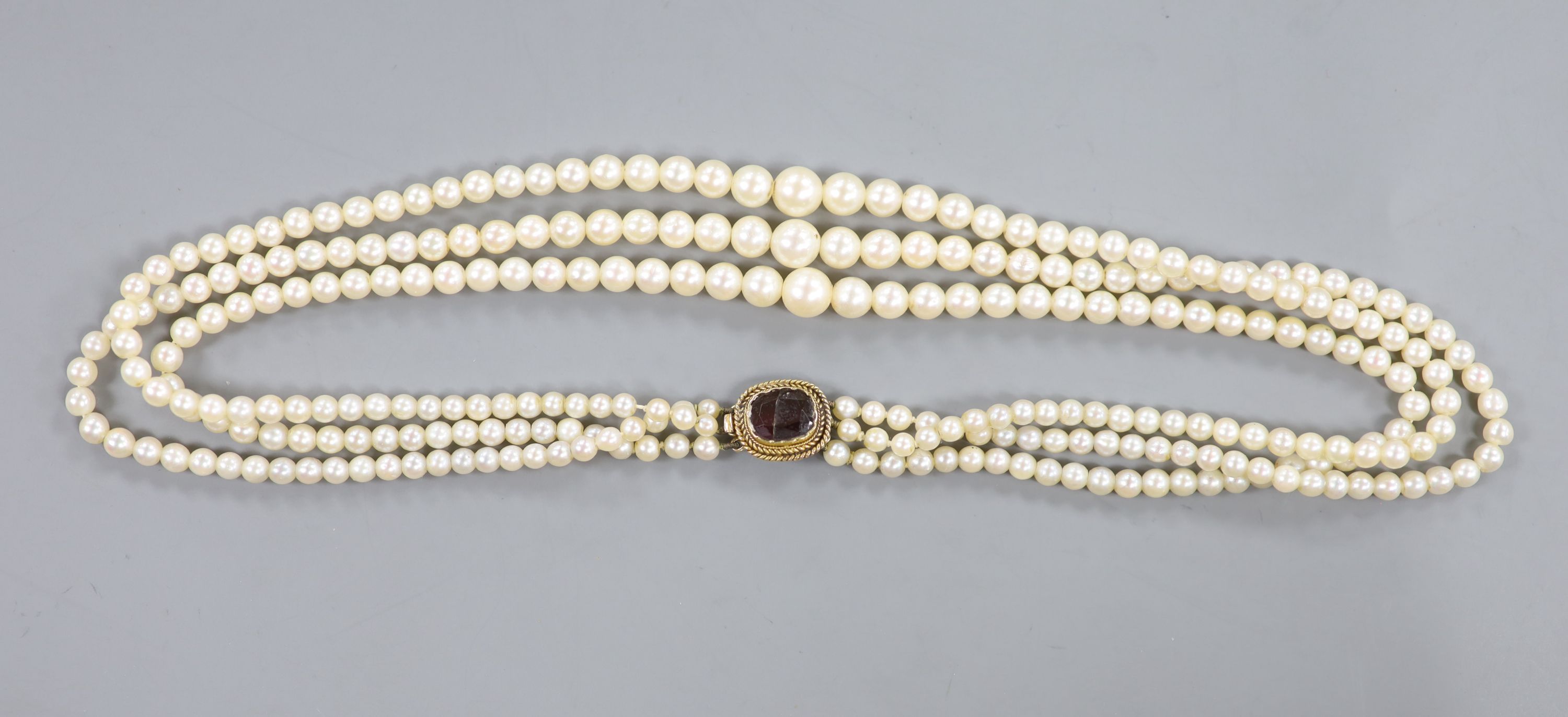 A triple strand graduated cultured pearl choker necklace, with yellow metal and garnet(cracked) set clasp